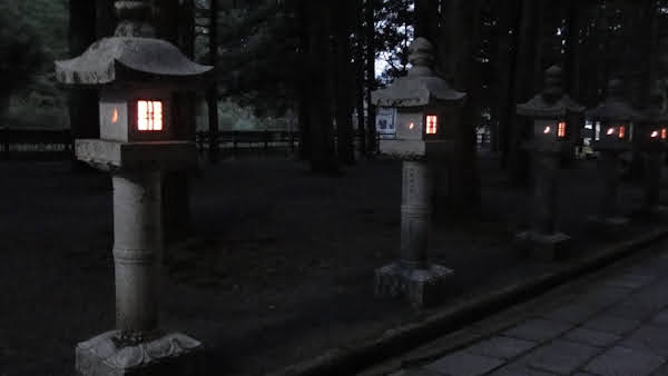 a line of several lit stone lanterns along the edge of a path at night